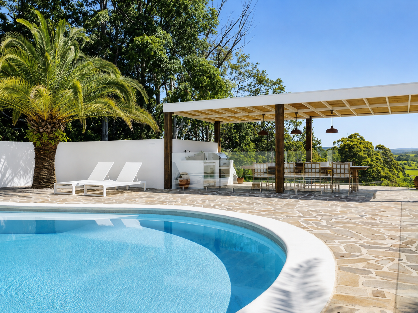Clunes pool pavilion in daylight — flagstone terrace, palms and glass pool fence with hinterland views