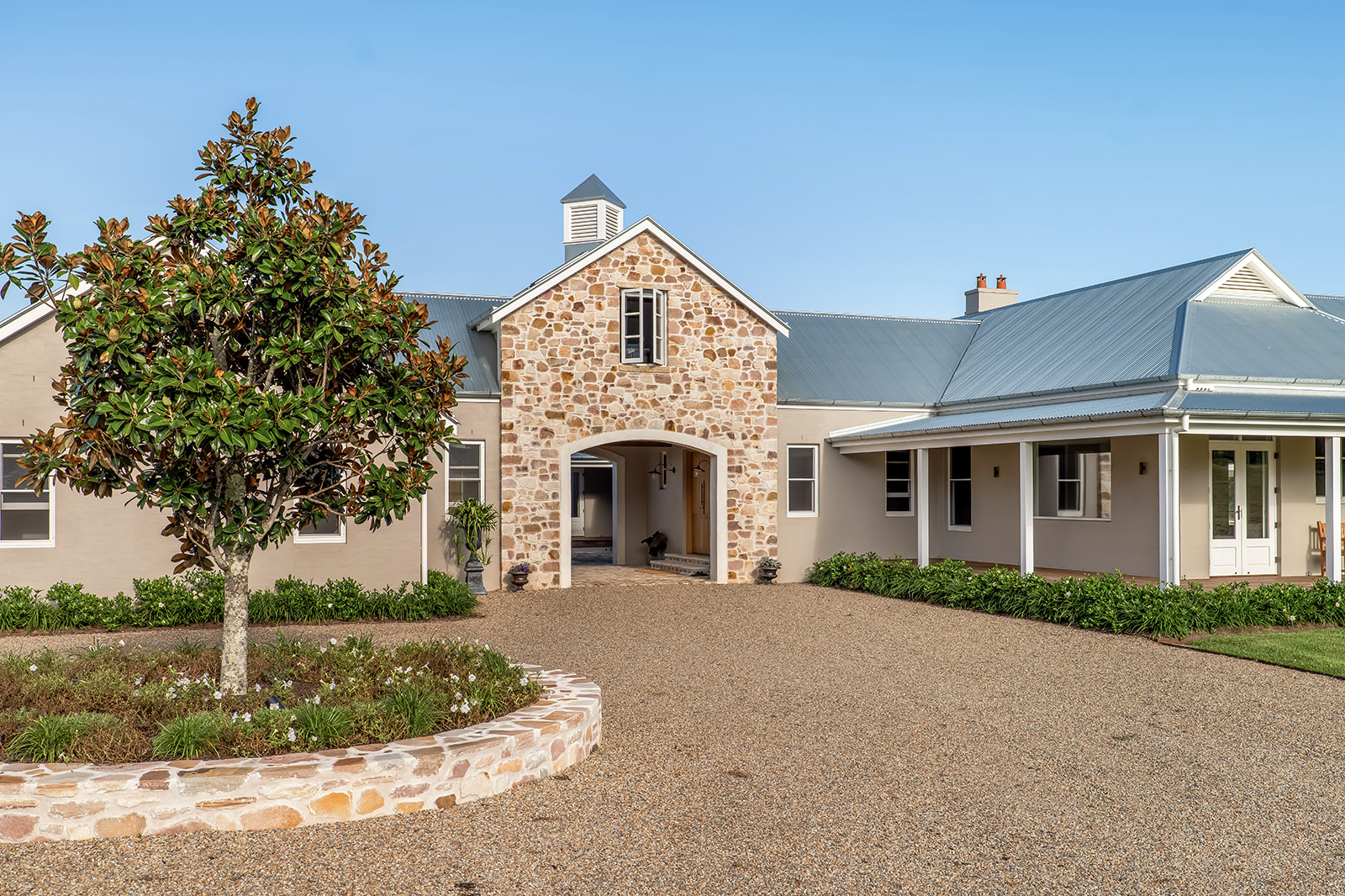 Rendered and stone homestead with arched stone entry, wide verandah and gravel driveway