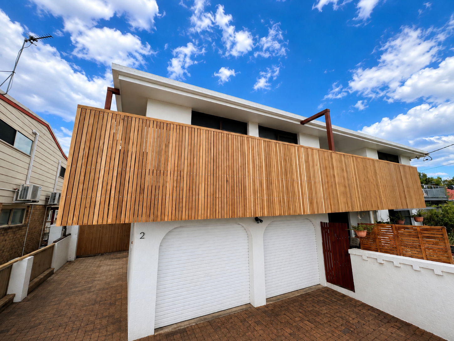 Deck construction in the Northern Rivers — two-storey home with a wide timber-slat balcony screen above a white double garage