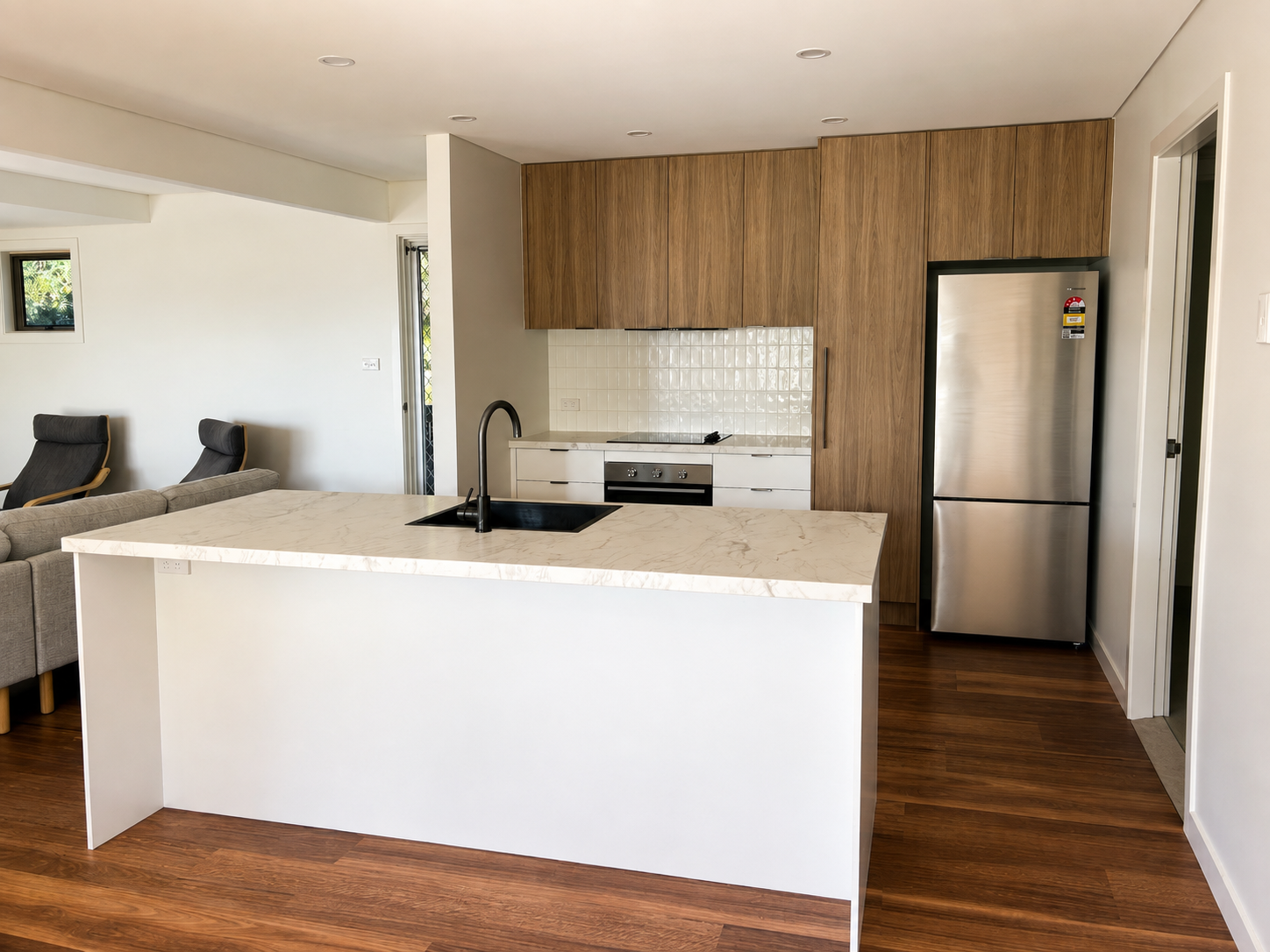 Northern Rivers home renovation — open-plan kitchen with white waterfall island, wood-veneer cabinetry and stone benchtop opening to a living area