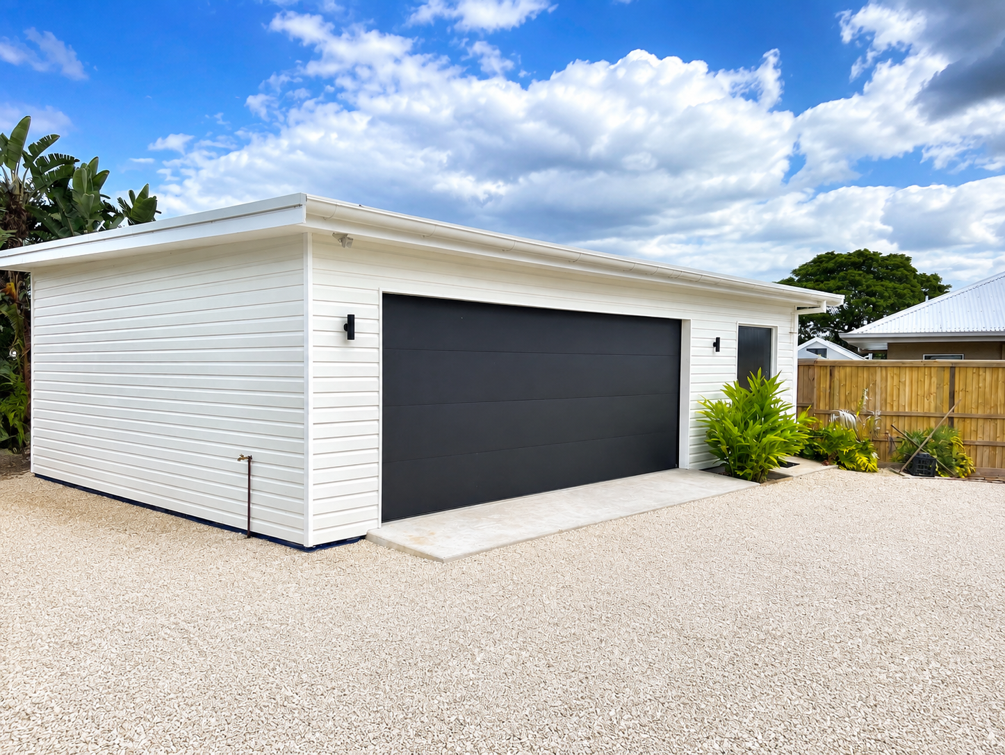 Home extension in the Northern Rivers — white-clad detached studio with black doors on a gravel apron and tropical planting