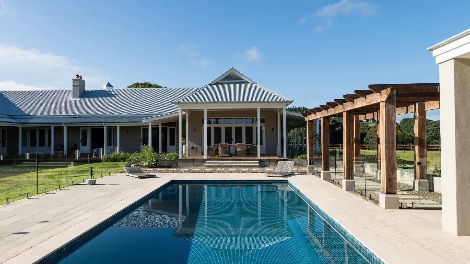 Rear of the Possum Creek residence overlooking a rectangular swimming pool with a timber pergola and lounge deck