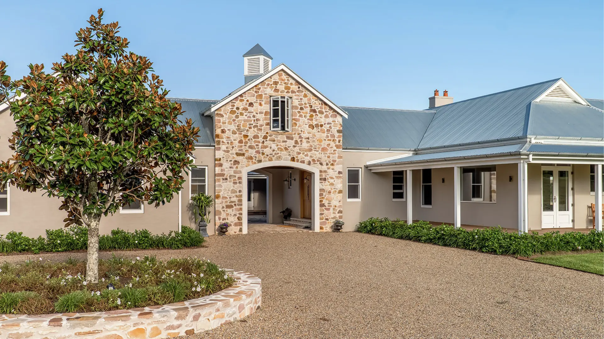 Front entrance of the Possum Creek residence with a stone-clad gable, arched breezeway and magnolia tree